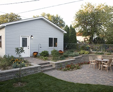 Gray home after paver patio installation with retaining wall planting area