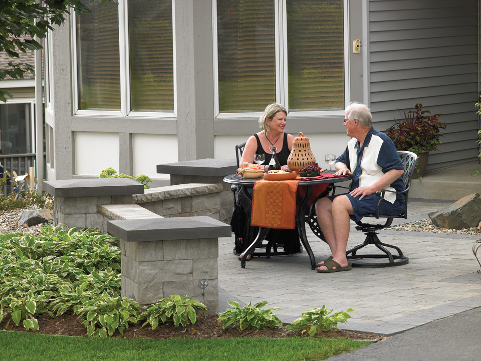 Older couple enjoying wine on a Gray stone paver patio with angled Brisa freestanding walls 