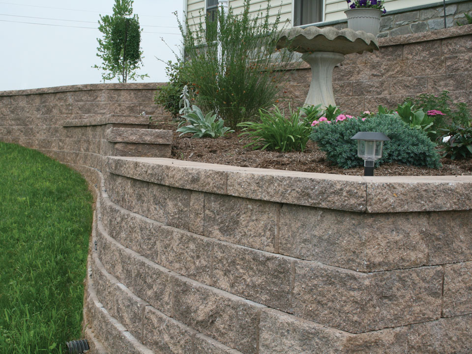Close view of a raised Diamond Pro straight face retaining wall planting area with stone bird bath