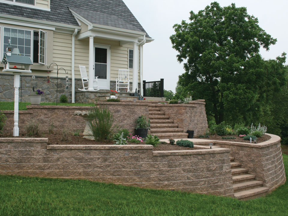 White home with raised curved and terraced Diamond Pro straight face retaining wall planters and stone staircase