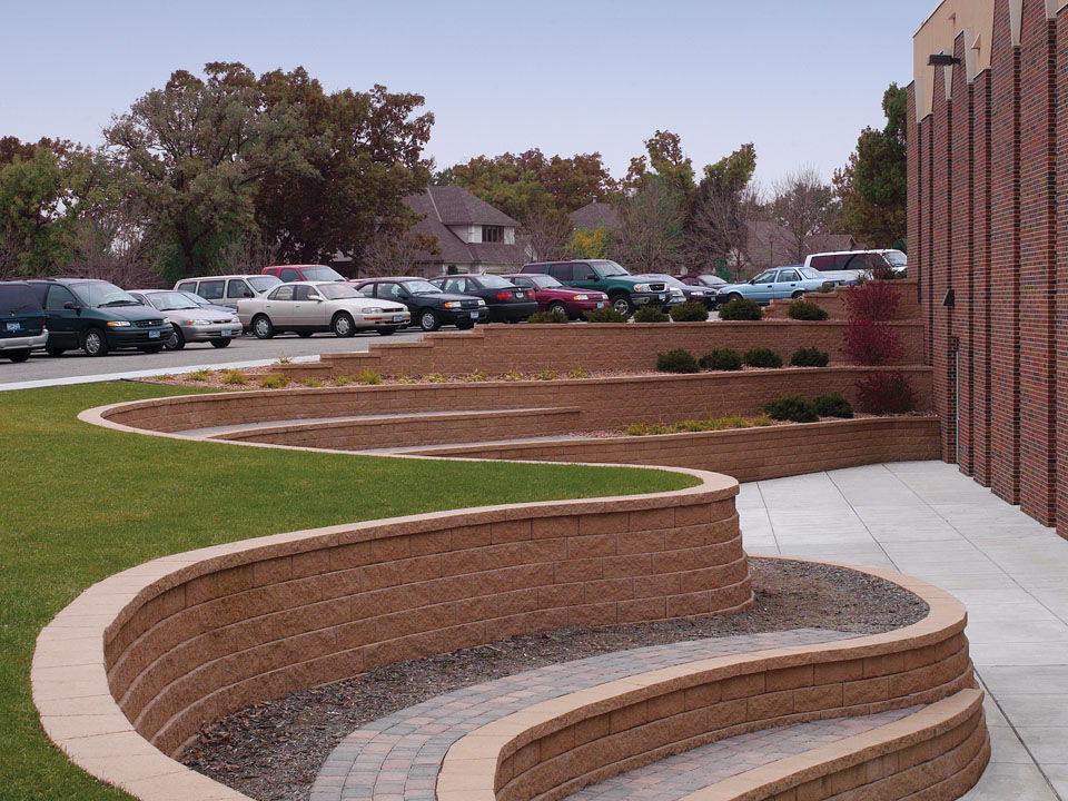 Parking lot edged by a curved and terraced Diamond Pro straight face concrete block retaining wall