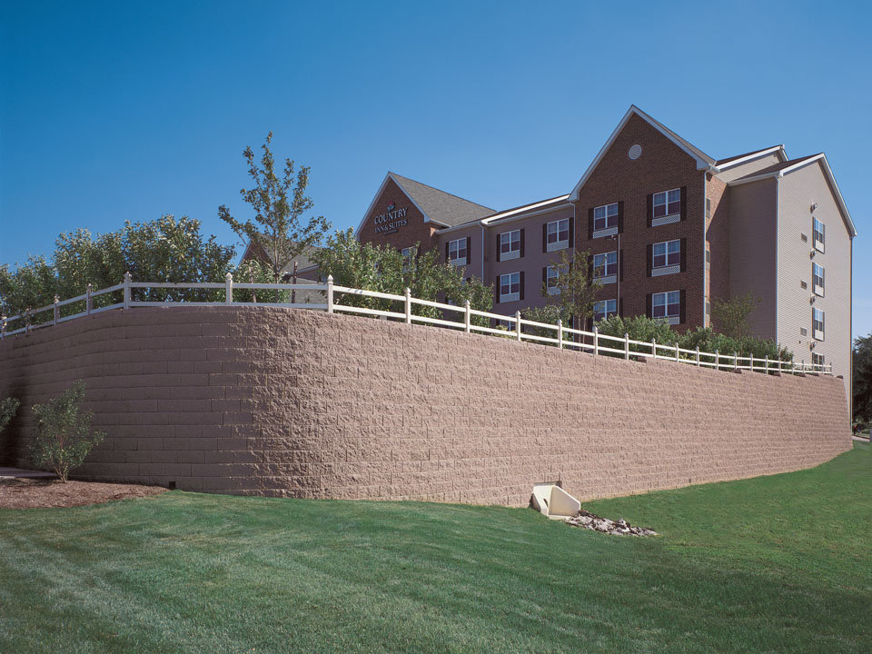 Country Inn and Suites surrounded by a curved Diamond Pro straight face concrete block retaining wall topped with a white fence