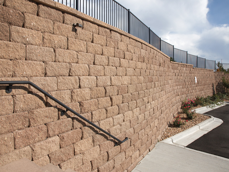 Close view of a curved Diamond Pro stone cut concrete block retaining wall topped with a black metal fence