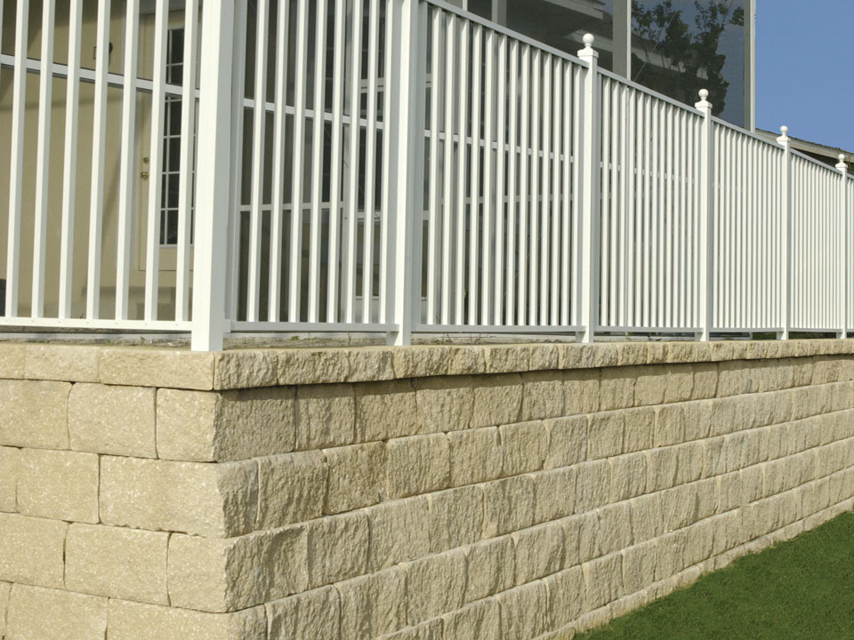 Close corner view of a Diamond Pro stone cut retaining wall topped with a white fence