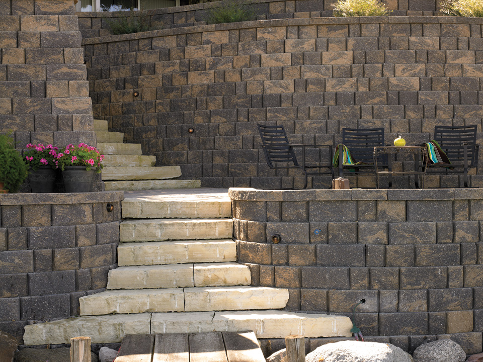 Diamond Pro stone cut concrete block curved and terraced retaining walls with a white block staircase and black patio furniture 
