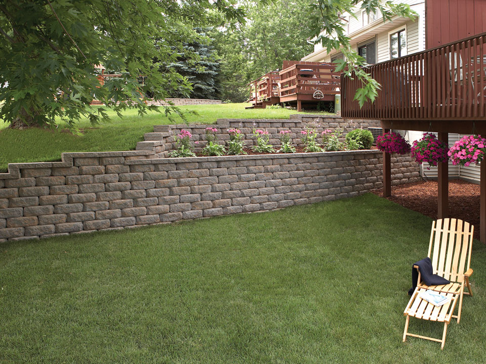 Back yard with a wood deck and raised terraced Diamond Pro stone cut casual face retaining wall planting area