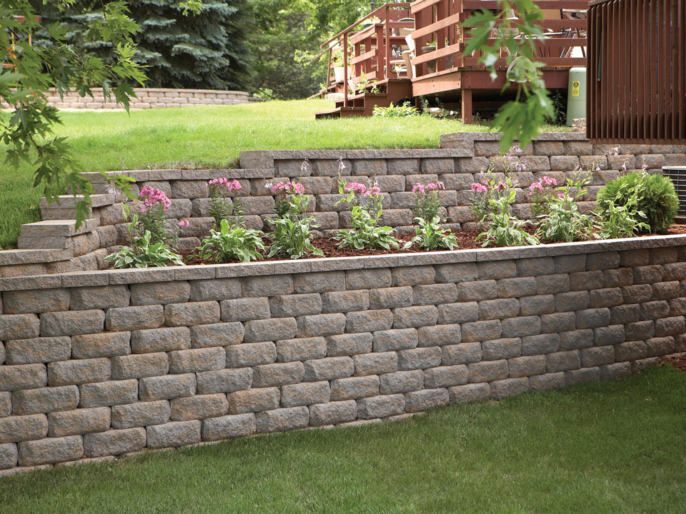 Close view of terraced Diamond Pro stone cut casual face retaining wall planting area with pink lilies