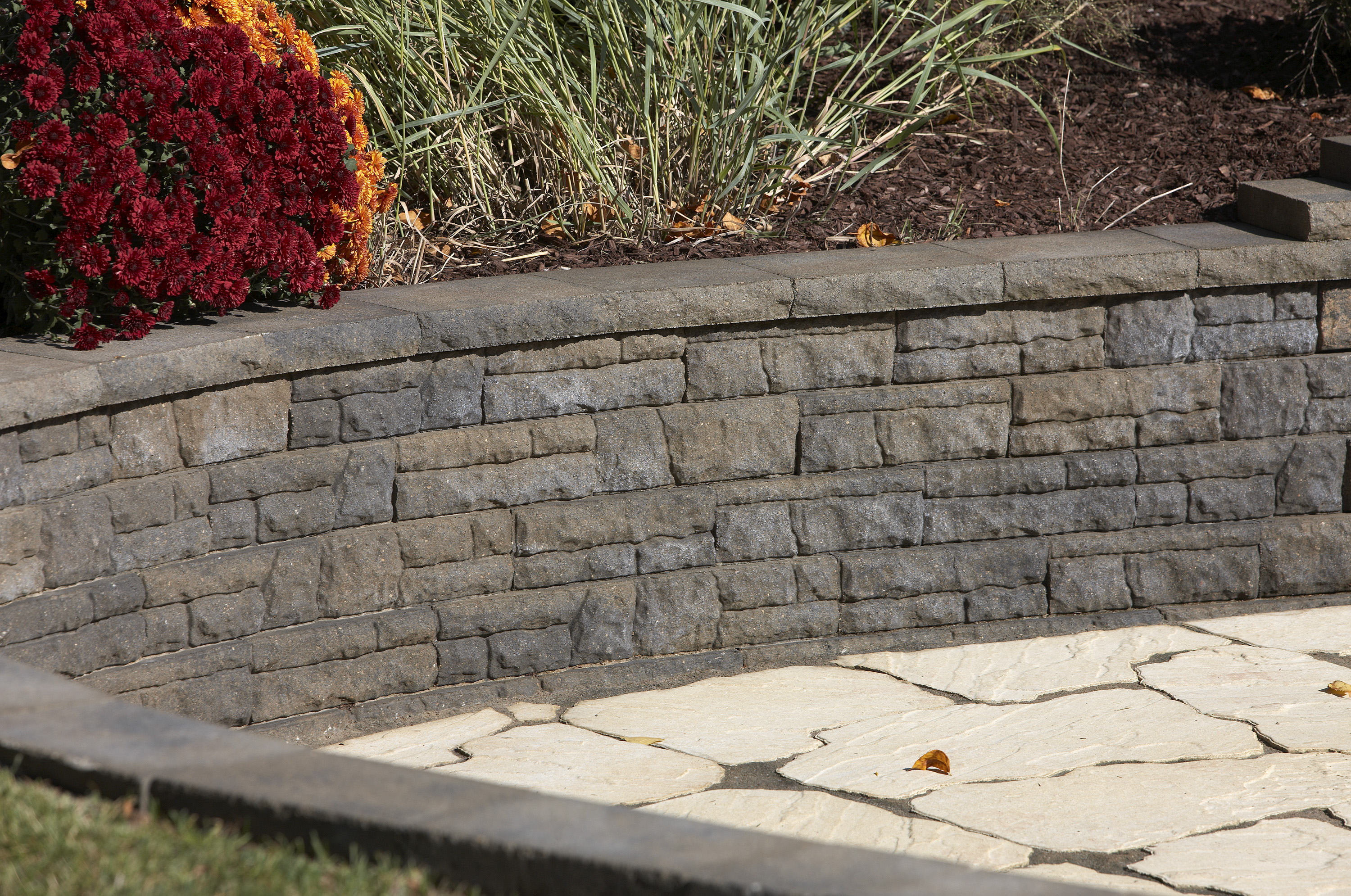 Close view of a curved high walled raised Flores concrete retaining wall planter with red and orange flowers