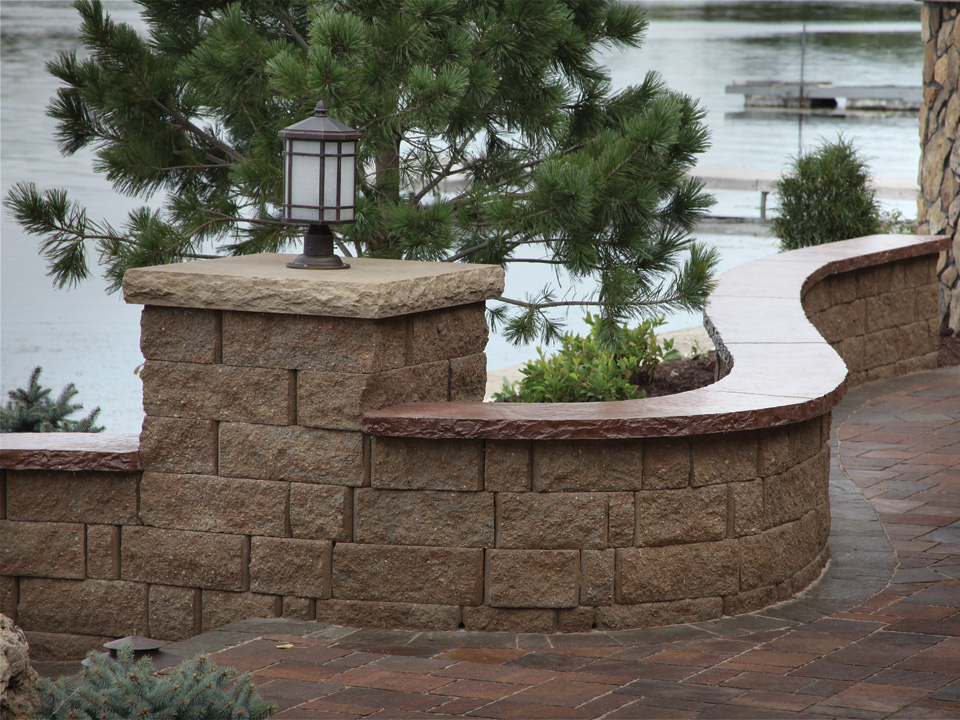 Close view of a curved capped freestanding concrete block wall and column topped with a black lantern light feature