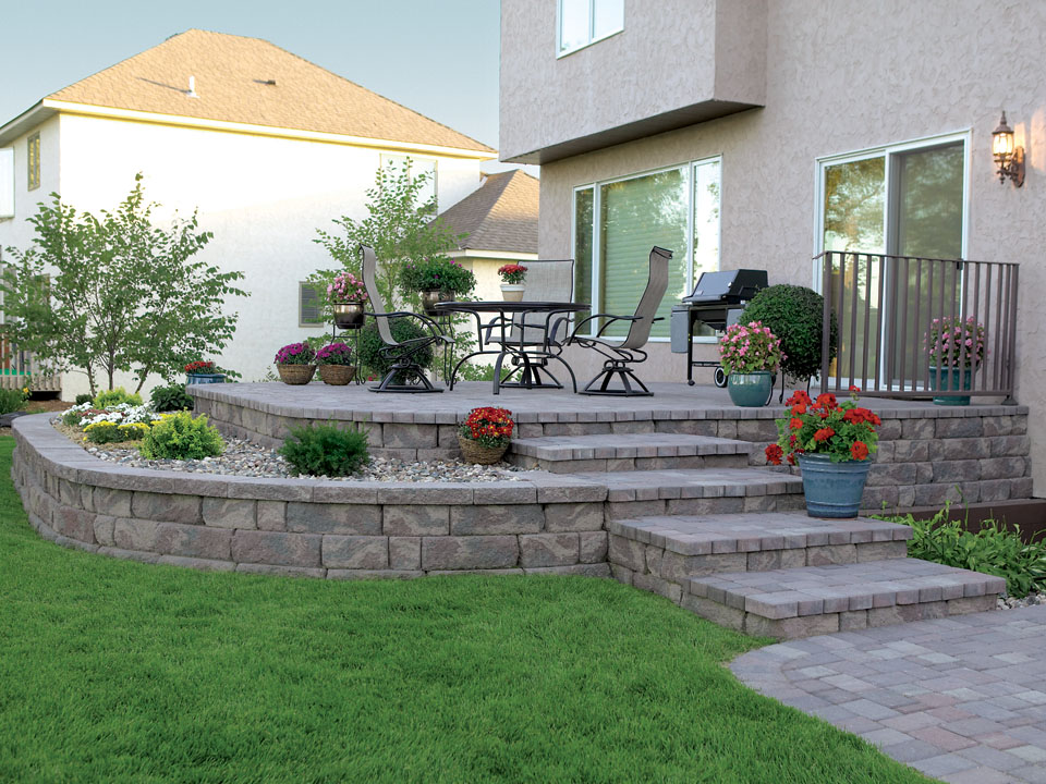 Raised backyard paver patio with curved raised Highland Stone concrete block retaining wall planters and built-in steps