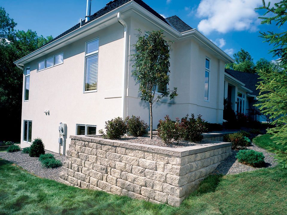 Rear corner of grey home with square raised Highland Stone concrete block retaining wall planter