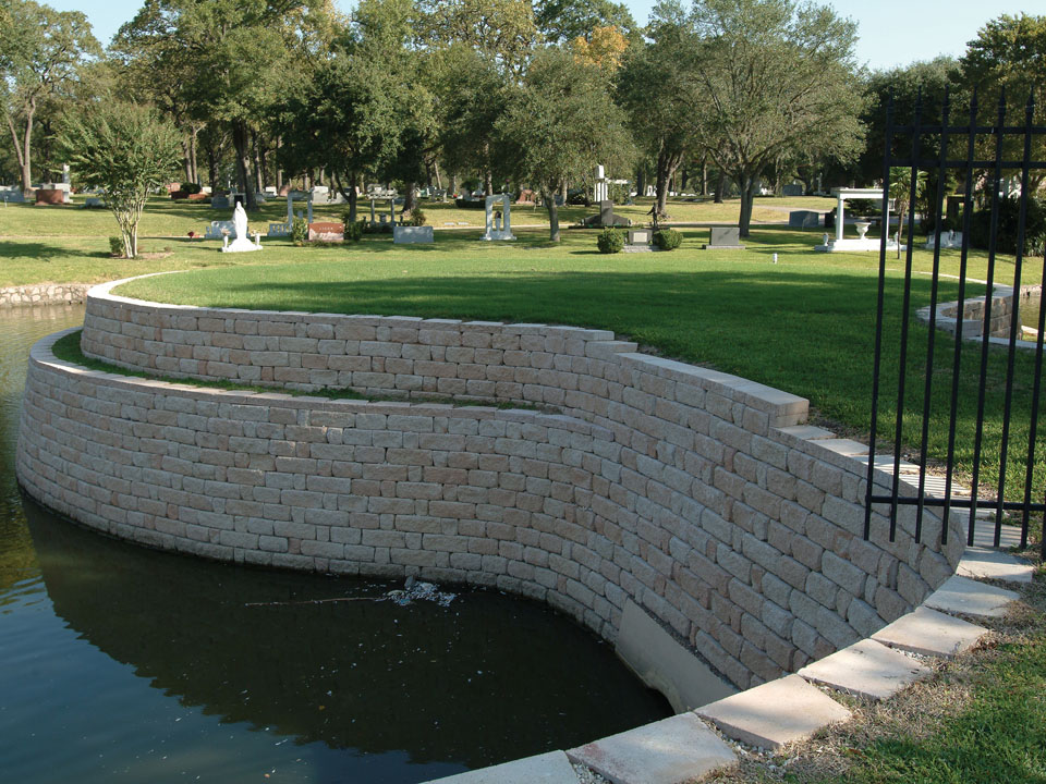 Corner view of cemetery and water feature separated by a curved terraced Highland Stone concrete block retaining wall