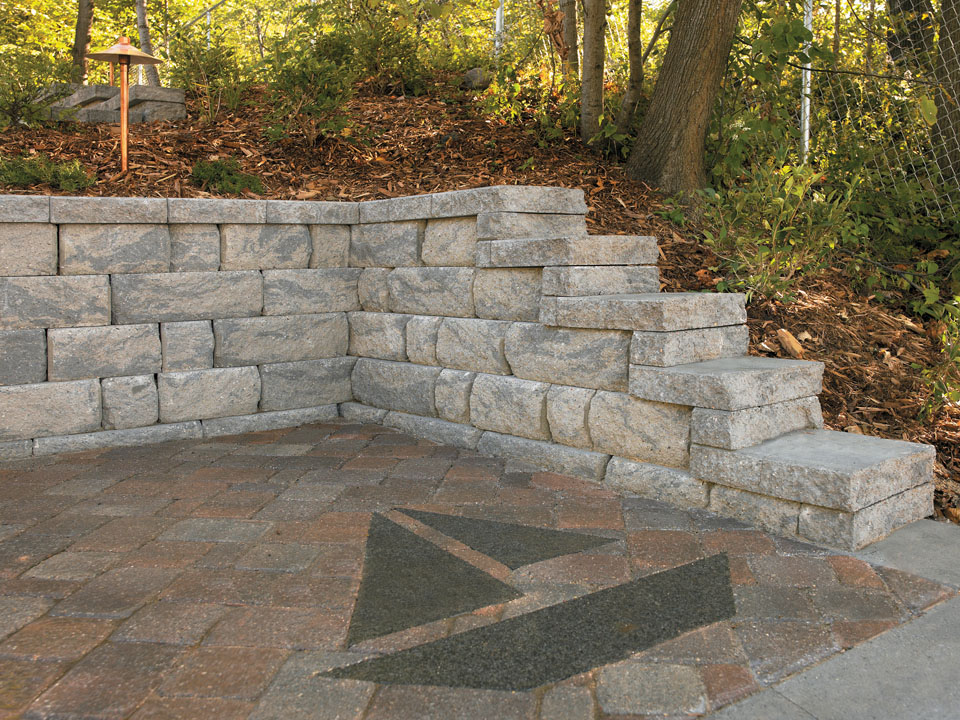 Corner of a paver patio with inset sailboat design, surrounded by stepped Highland Stone concrete block retaining walls