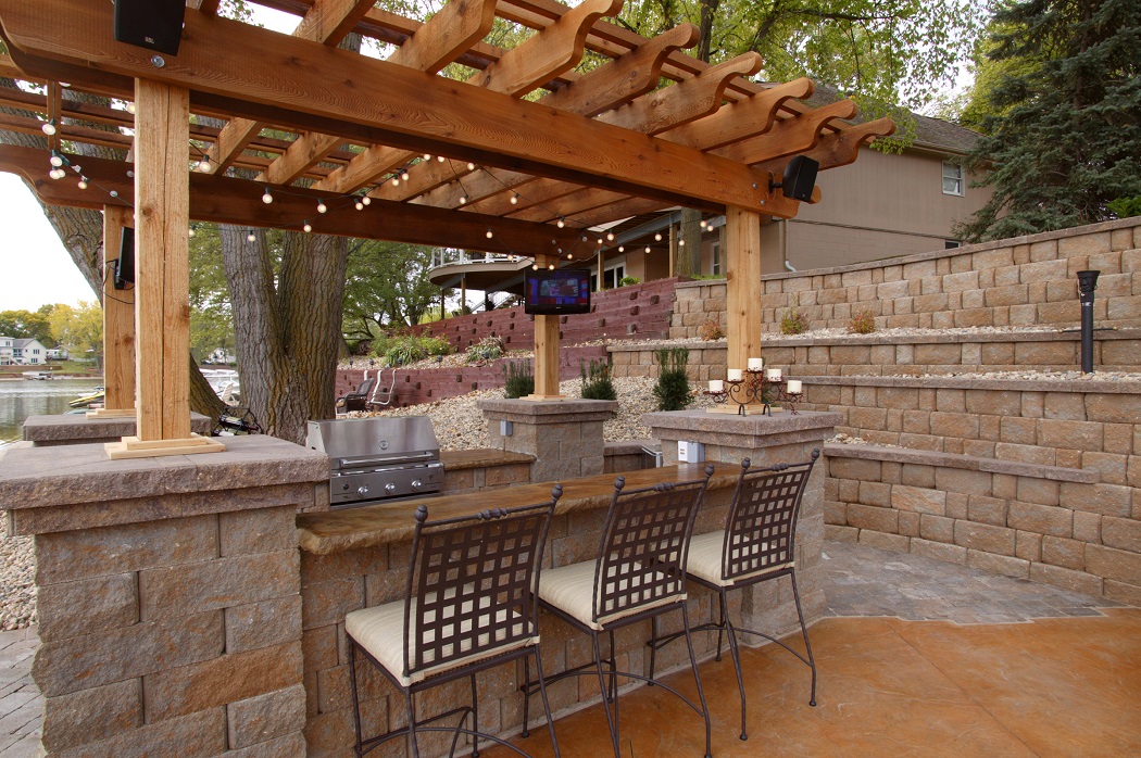 Paver patio grilling area with built-in bar concrete block columns and wooden pergola, surrounded by terraced retaining walls