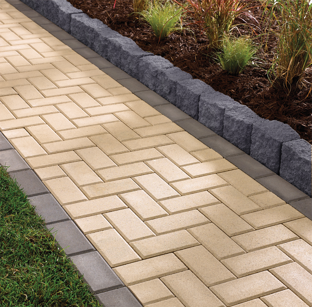Close view of dark gray Highland Stone landscape concrete block edgers flanking a two-tone concrete paver walkway. 