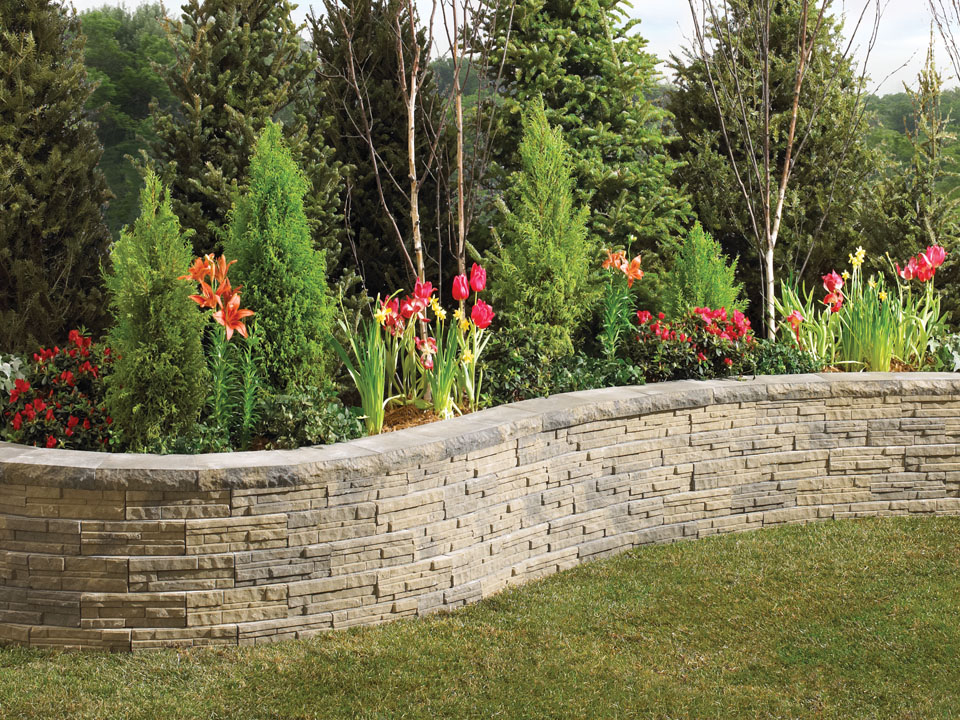 Curved raised planter with tulips, lilies, and shrubs, made from LedgeWall concrete retaining wall blocks.