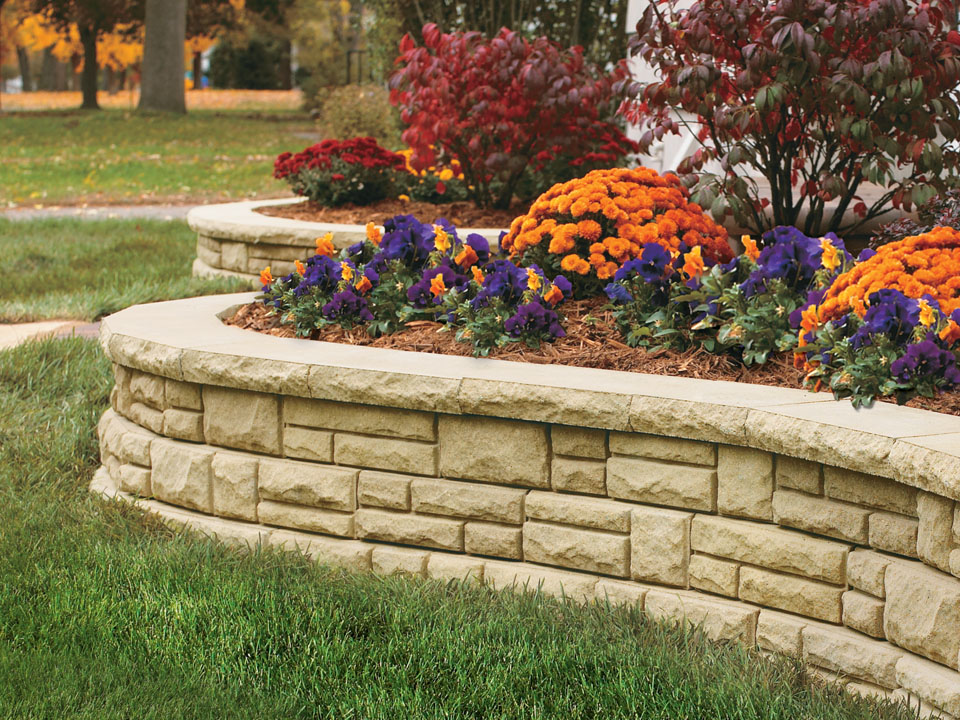 Close view of a curved Natural Impressions Ashlarstone concrete block retaining wall planter with orange and purple flowers. 