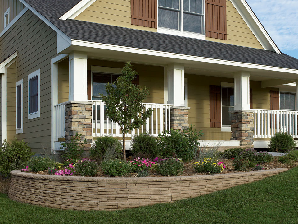 Front porch of a brown house with a curved raised Natural Impressions Flagstone concrete block planter. 