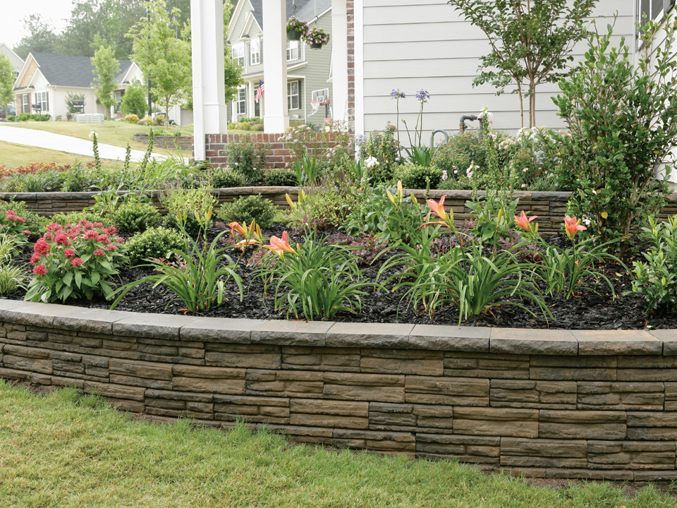 Close view of lilies planted in a raised curved Natural Impressions Flagstone concrete block planter. 