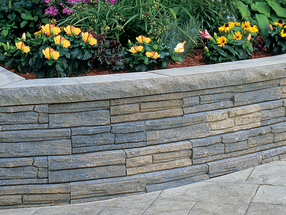 Close view of a raised Natural Impressions Flagstone concrete block planter with yellow flowers on a paver patio. 